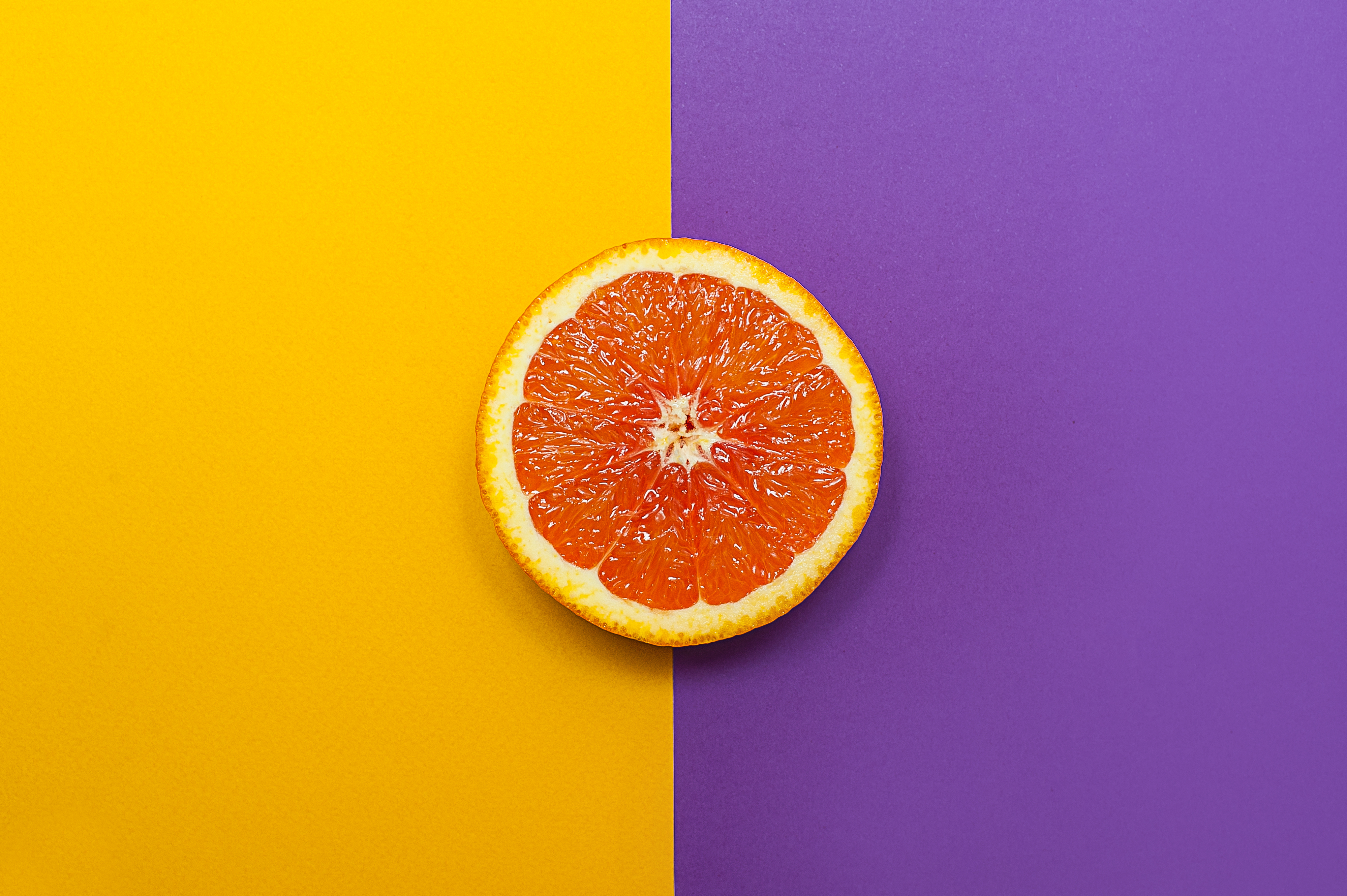 Un'arancia tagliata a metà che mostra la sua struttura interna, posta su una superficie divisa in due colori contrastanti, giallo e viola.