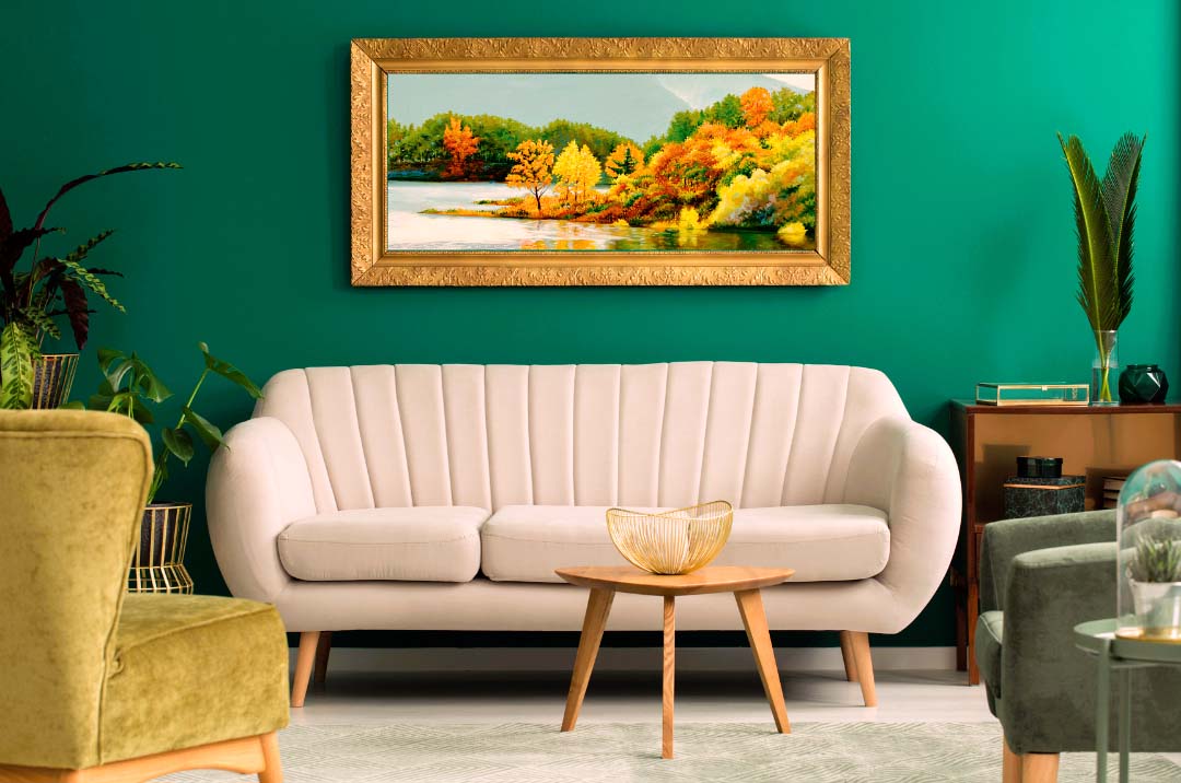 Soggiorno accogliente con parete verde scuro, divano moderno color crema con scanalature e poltrone verdi, completato da un grande quadro paesaggistico con colori autunnali che richiamano la natura.
